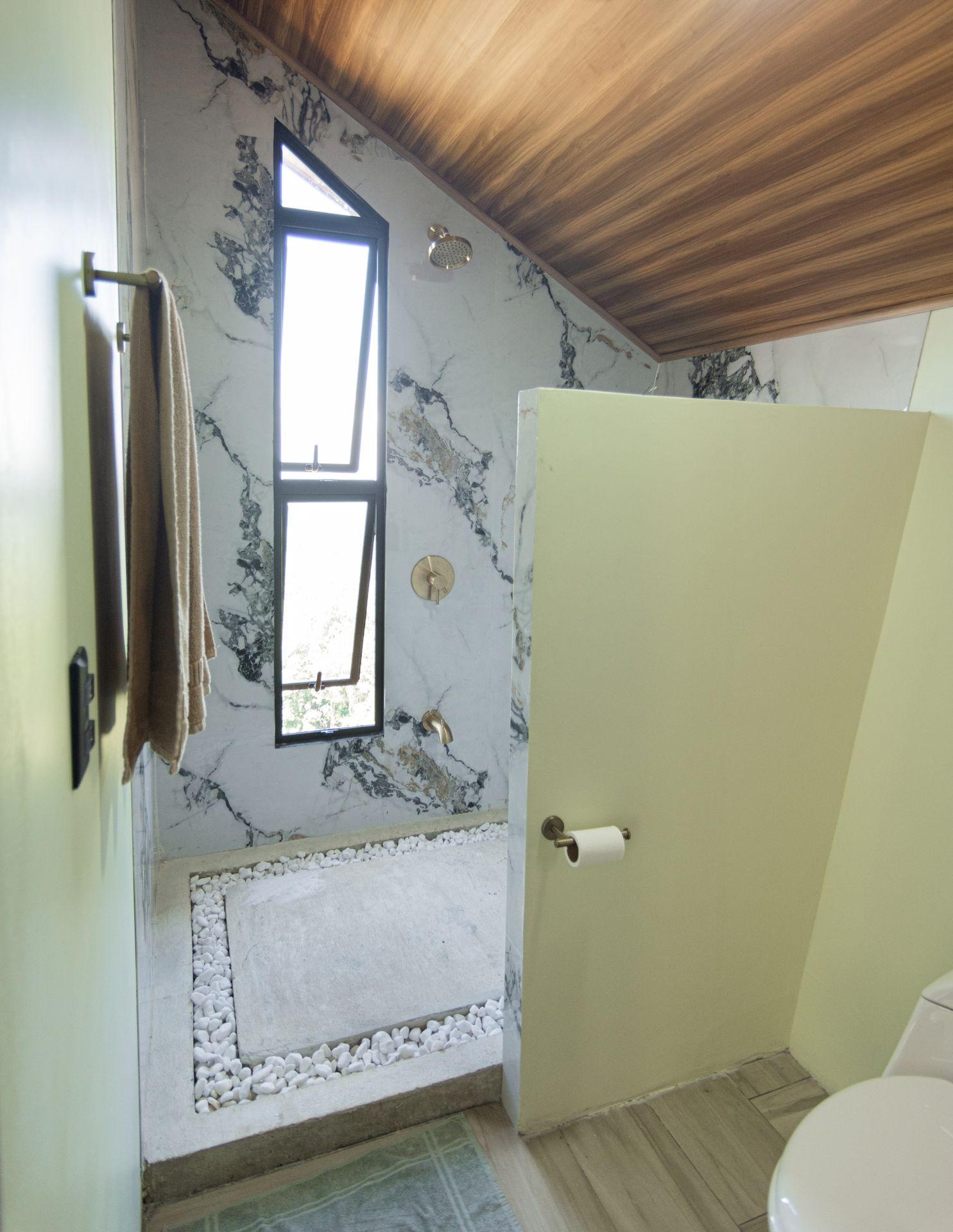 Baño con ducha de mármol, ventana triangular y piedras blancas