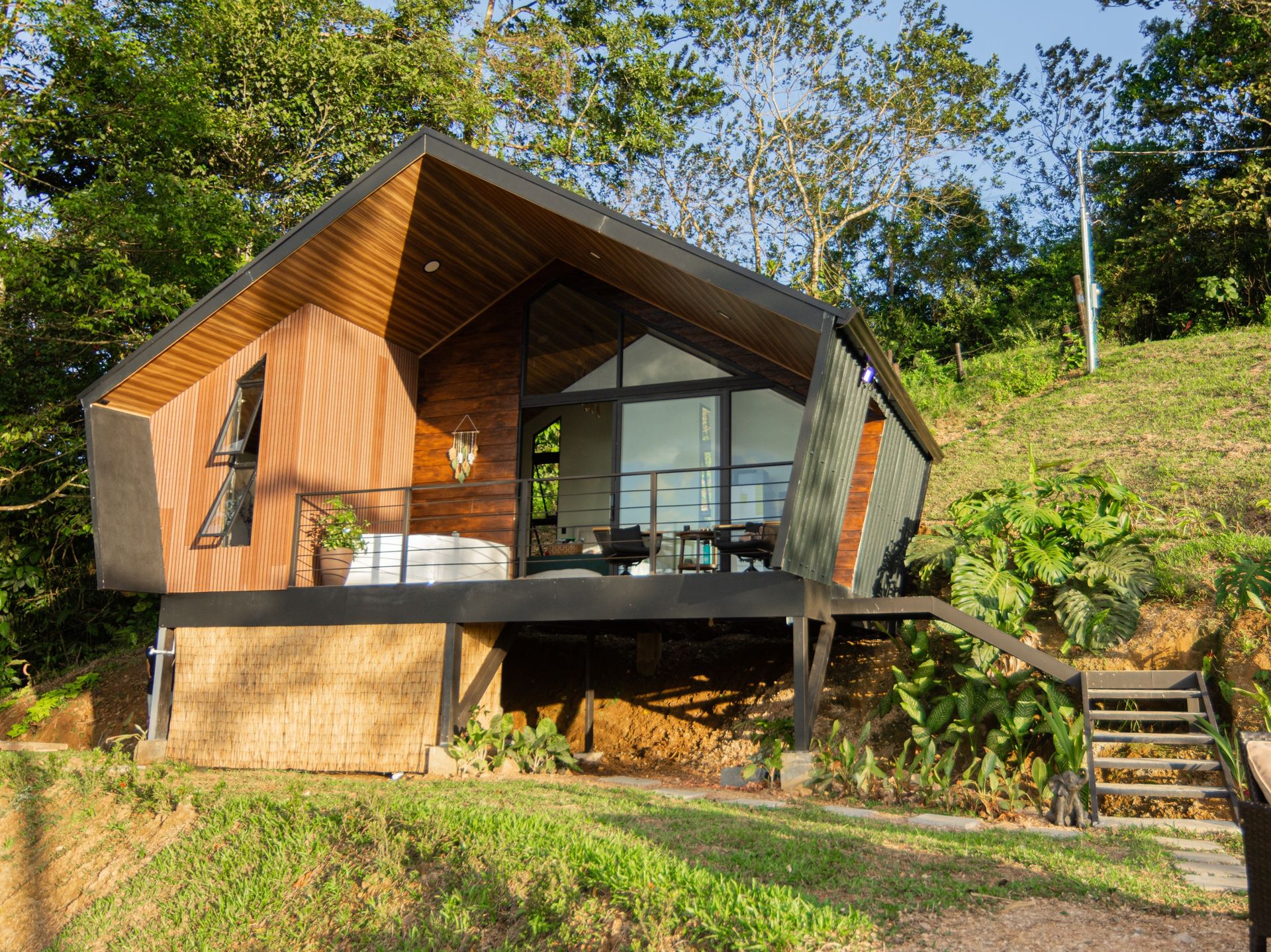 Cabaña Elevant Sanctuary de madera y metal con balcón y jacuzzi, rodeada de bosque tropical
